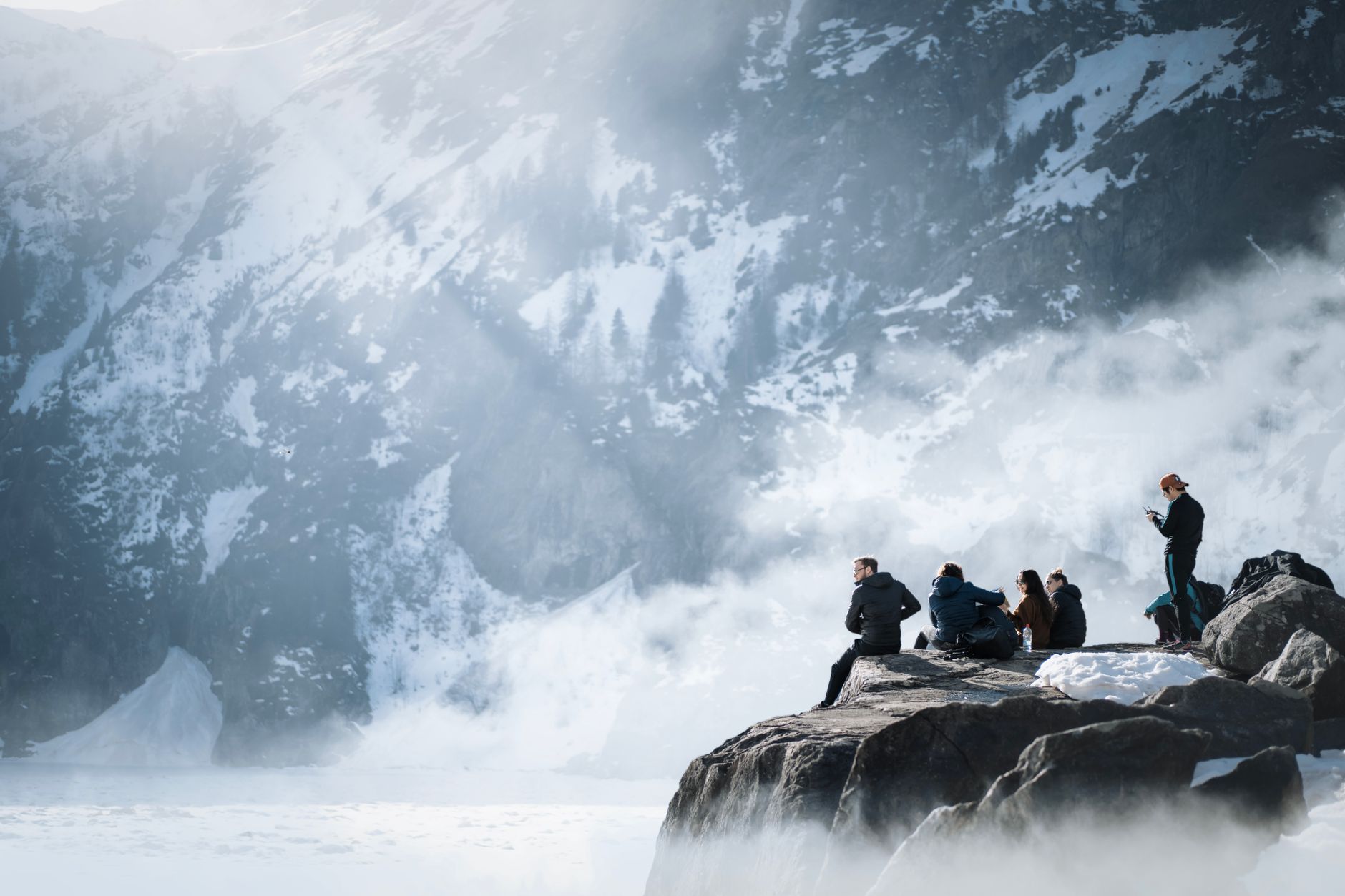 people sitting on a big rock wit ha view of a snow covered mountain